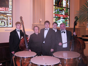 Photo: Galen, double base; Janet, Chorale; Aaron, timpani; Kelsey, Chorale; Bruce, double bass and mother with timpani and double basses - standing under stained glass windows